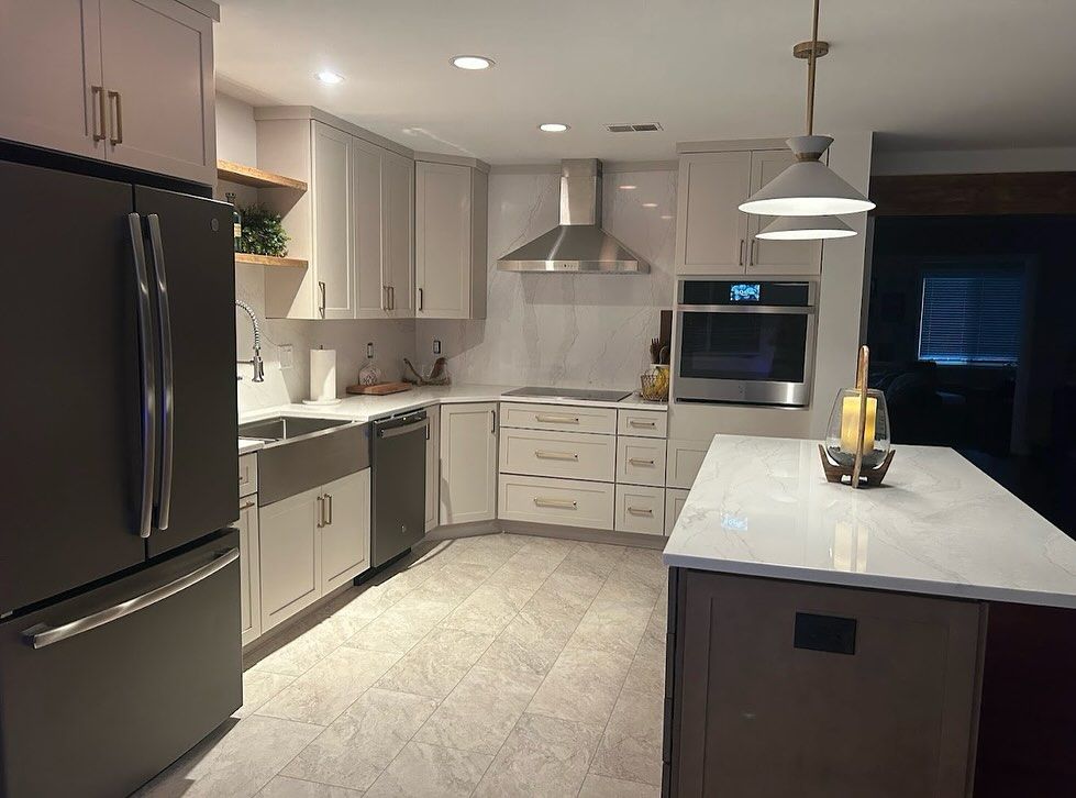 L-shaped kitchen makeover with light gray shaker cabinets, quartz counters and a chimney range hood
